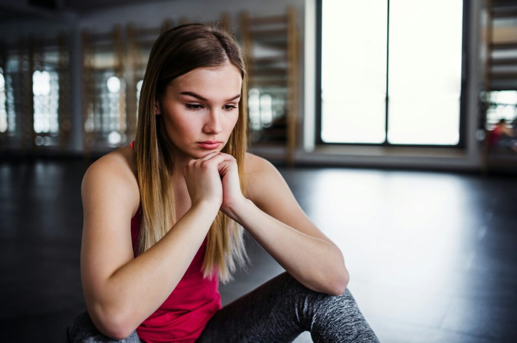 Woman in pink top looking at the ground with her hands folded.